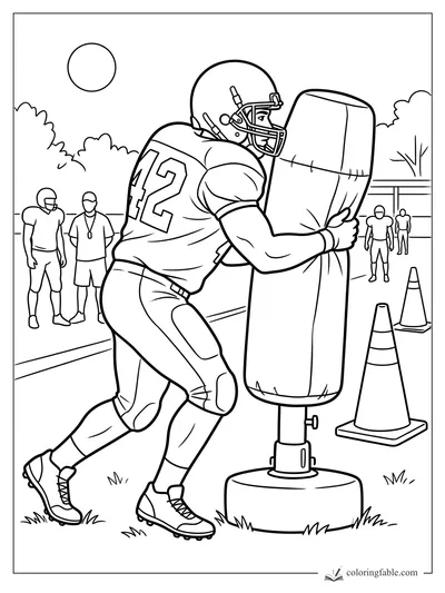 Football player number 42 driving into a padded blocking dummy during practice with cones and teammates nearby
